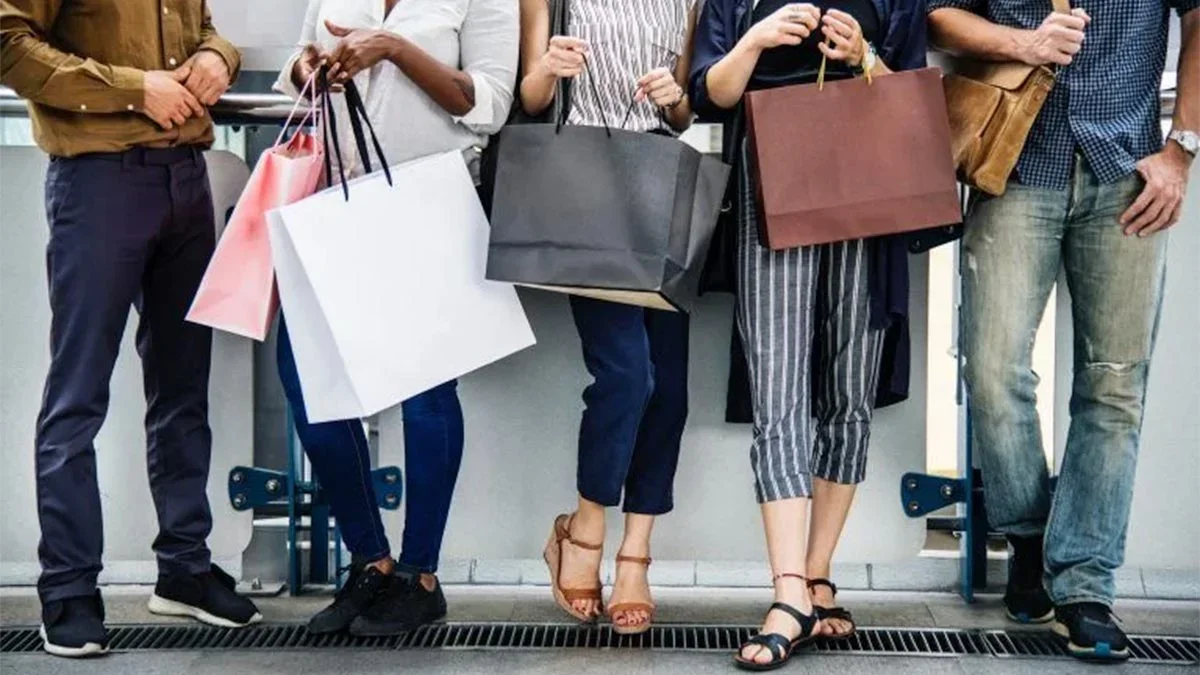 close up of women holding shopping bags standing against a wall